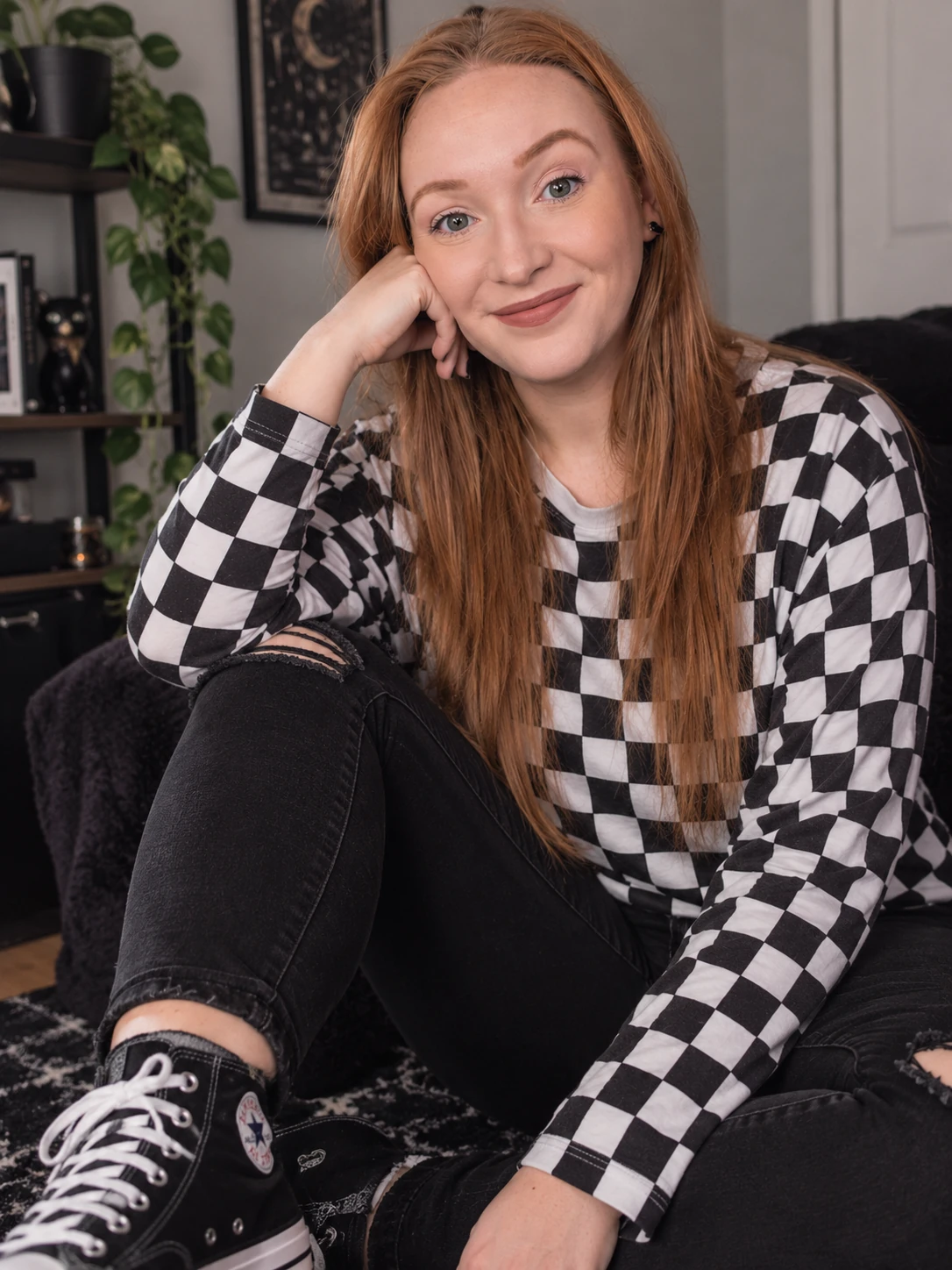 Christina smiling at home in a black-and-white checkerboard top and black Converse sneakers.